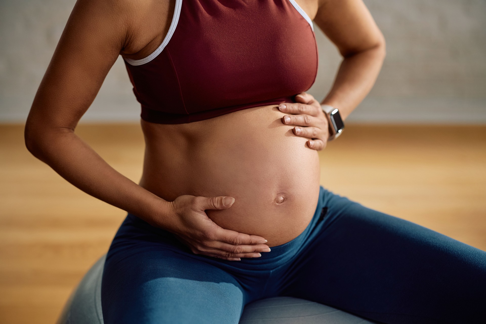Close up of sportswoman holding her pregnant stomach in health club.
